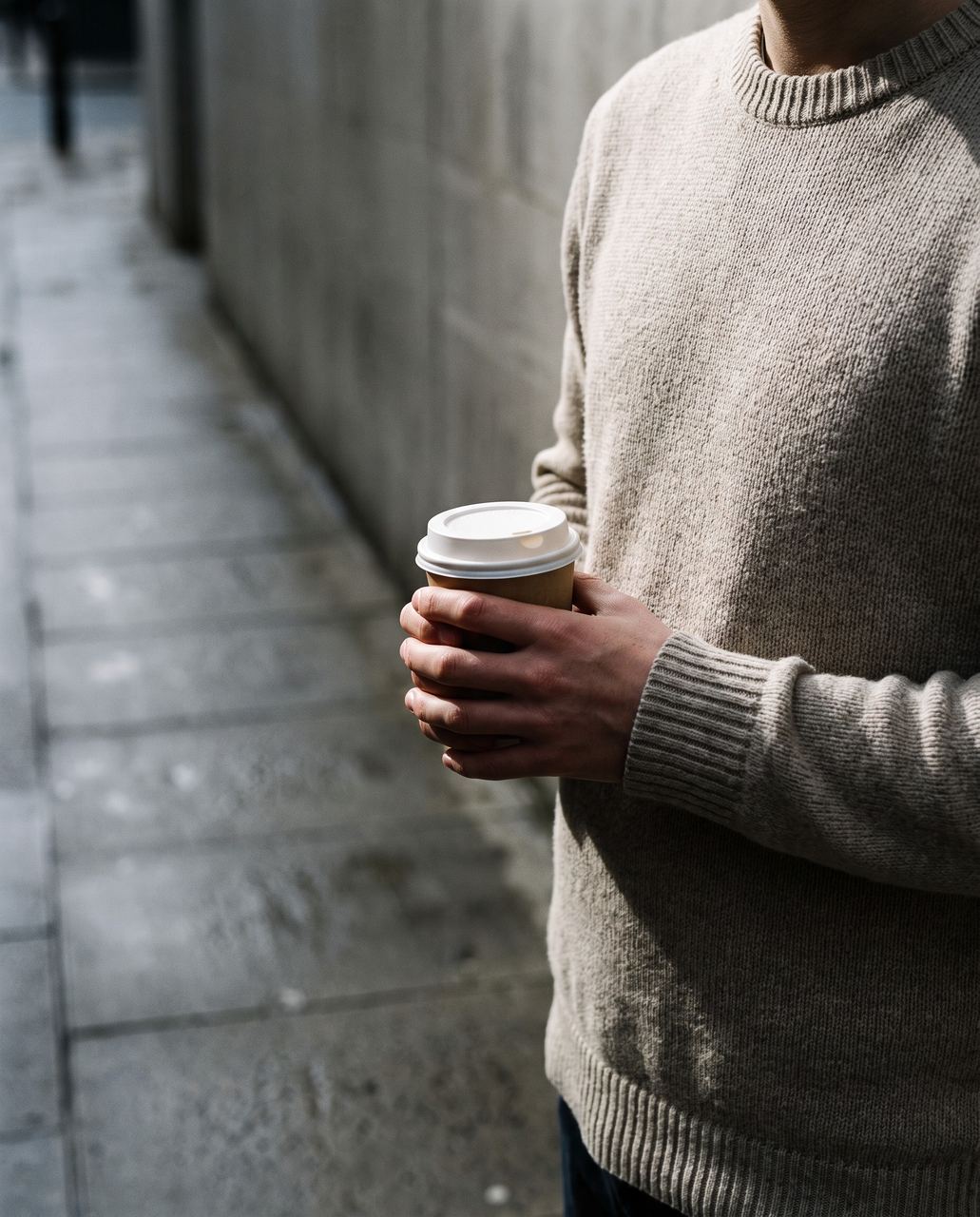 Une personne tient un gobelet de café, vue à hauteur de poitrine dans la rue.